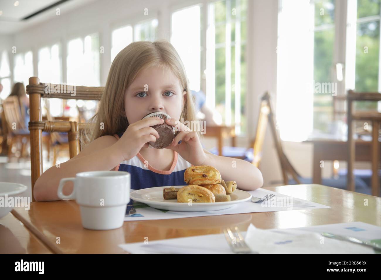Mignonne fille de 5 ans mangeant un muffin au chocolat au restaurant Banque D'Images