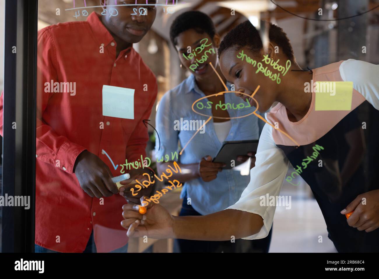 Heureux collègues afro-américains prenant des notes sur le mur de verre et discutant du travail dans le bureau créatif. Affaires, brainstorming et travail d'équipe, inchangés. Banque D'Images