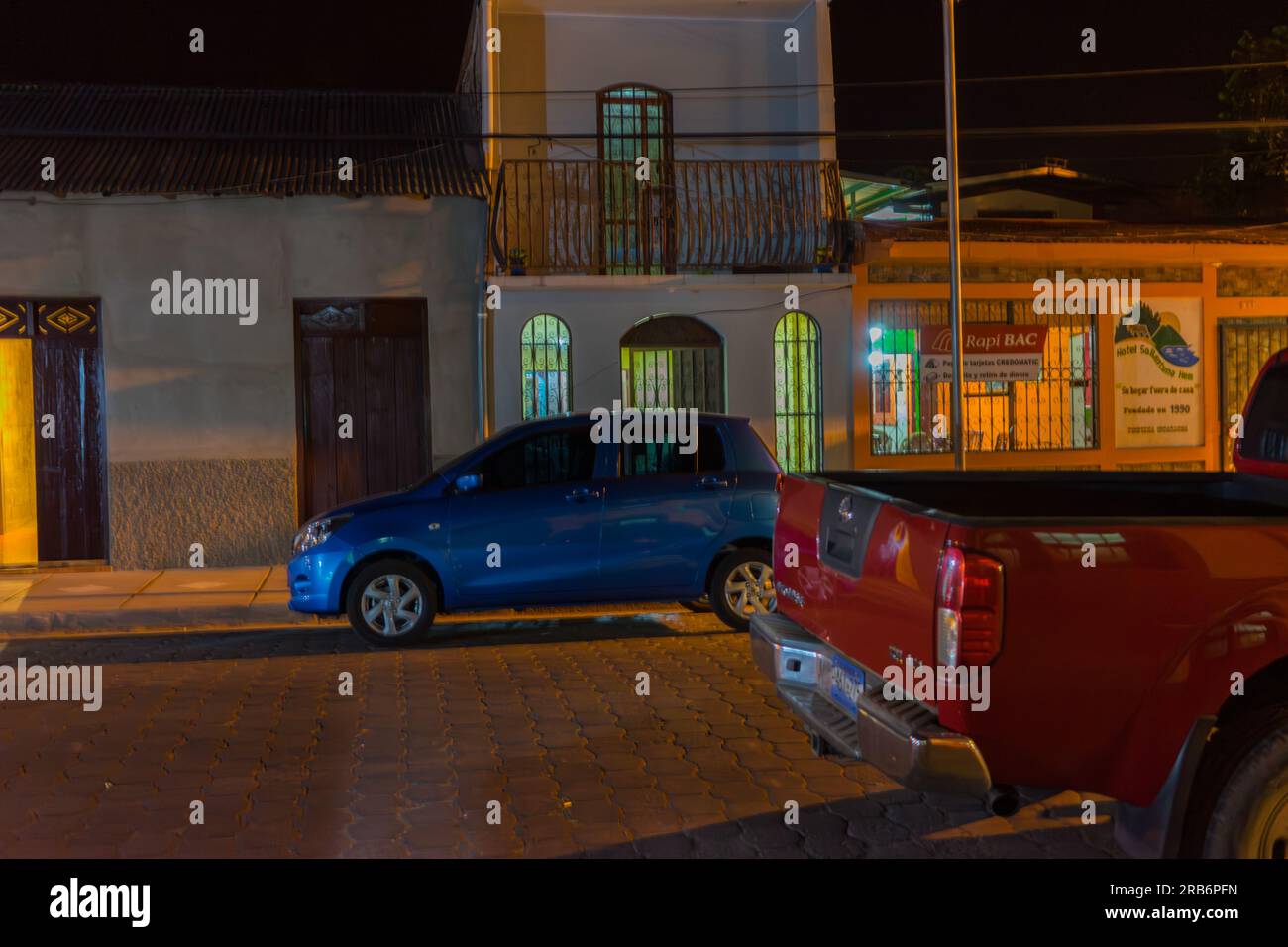 Une voiture compacte bleue et une camionnette rouge garées près d'un hôtel à Jinotega, Nicaragua, prises la nuit. Banque D'Images