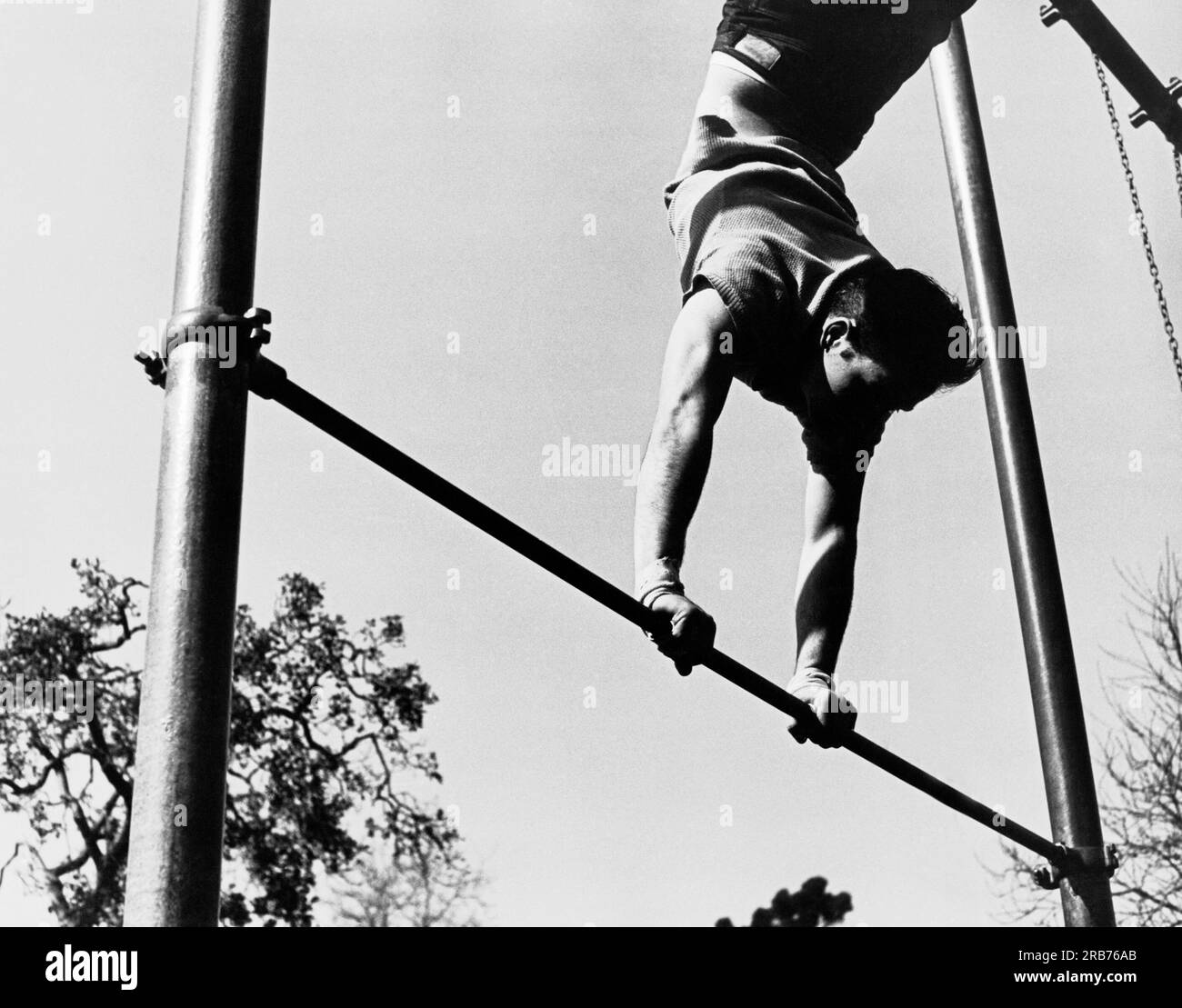 Californie : c. 1954 Un gymnaste masculin s'entraîne sur un support sur un bar à l'extérieur. Banque D'Images
