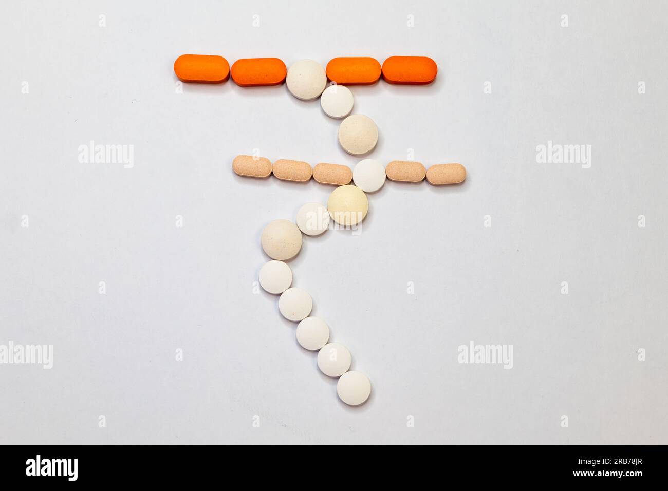 Une photo en gros plan de quelques pilules de soins de santé en forme de symbole de roupie indienne sur un fond blanc. Banque D'Images
