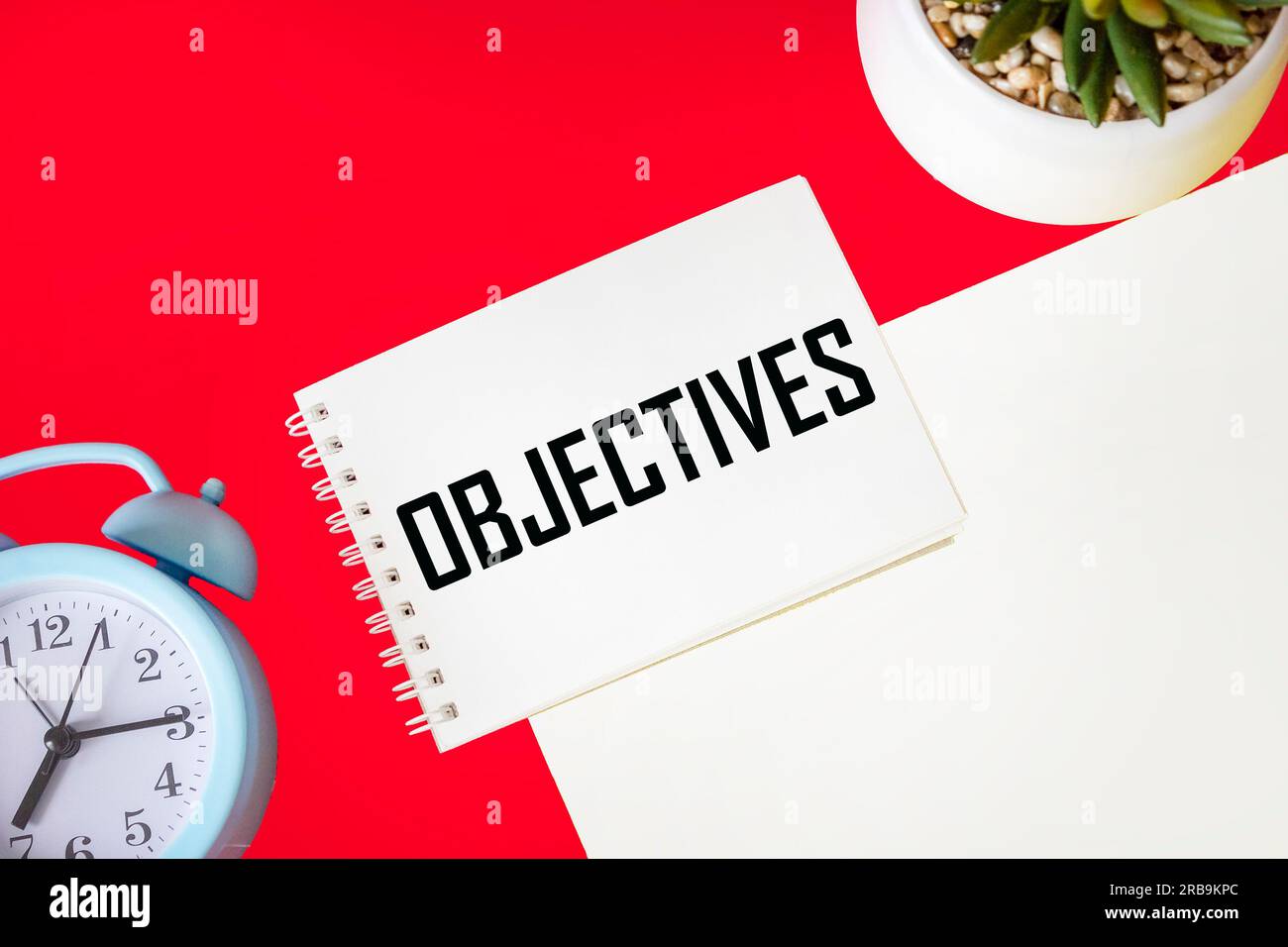 Les mots OBJECTIVES sont écrits sur un bloc-notes sur un fond blanc rouge avec une horloge Banque D'Images