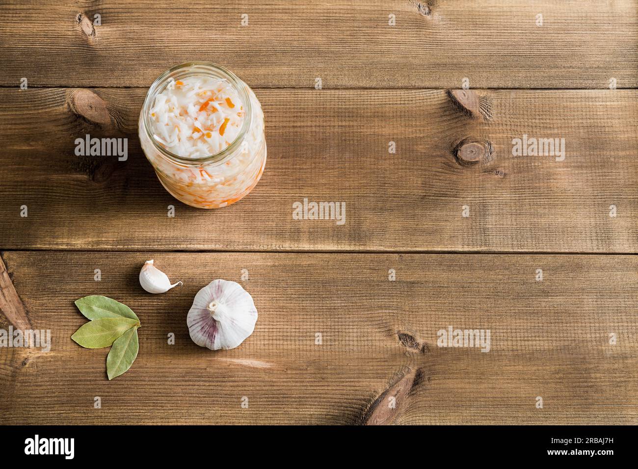 Choucroute maison dans le bocal en verre ouvert. À côté de l'ail et un peu de Laurier. Support de conteneur sur fond en bois. Aliment fermenté. Gros plan, pose à plat Banque D'Images
