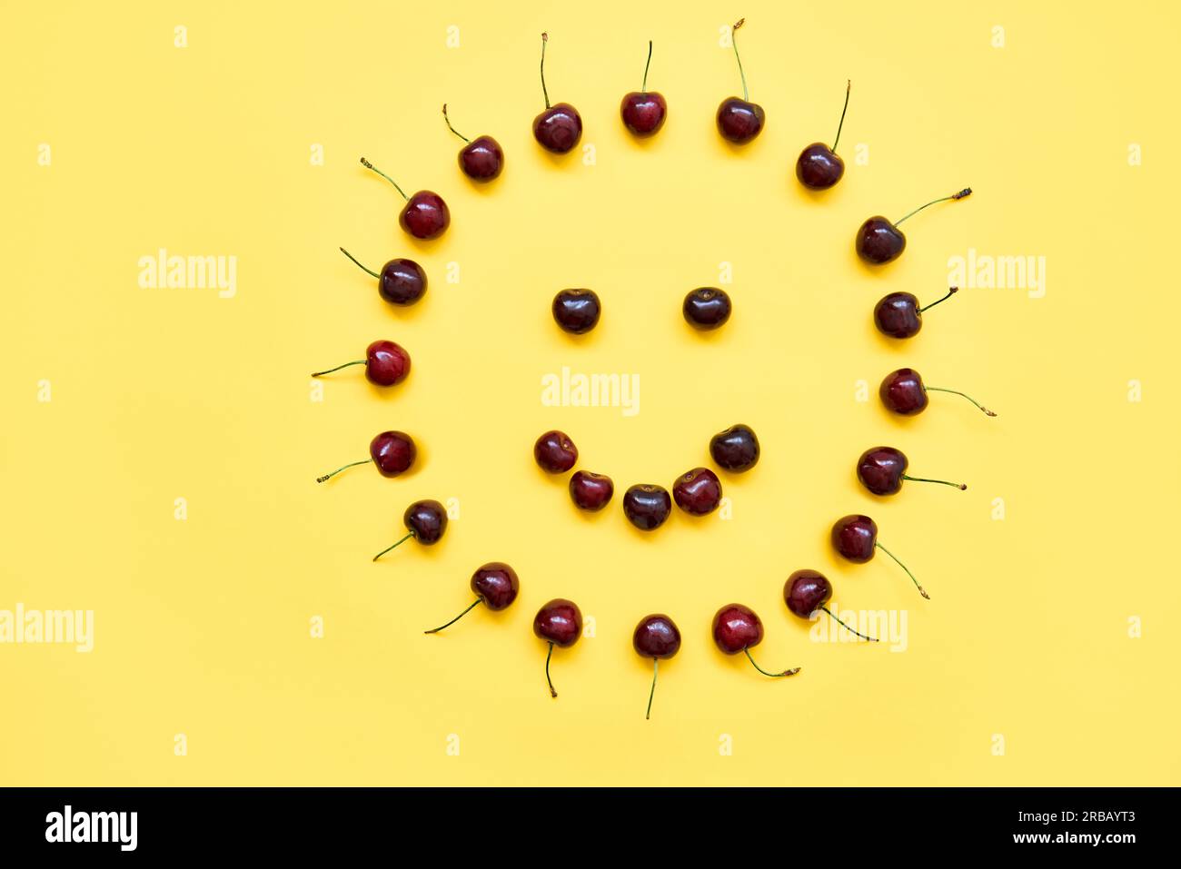 Visage souriant. Cerises douces sous forme de soleil sur fond jaune. Happy, fun, Food art concept Banque D'Images