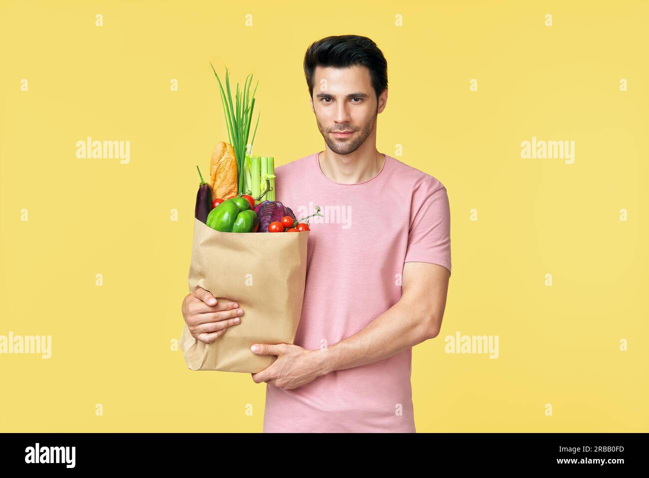 Jeune homme charmant tenant un sac de shopping en papier plein de légumes frais avec un espace de copie sur fond jaune. Concept de mode de vie sain Banque D'Images