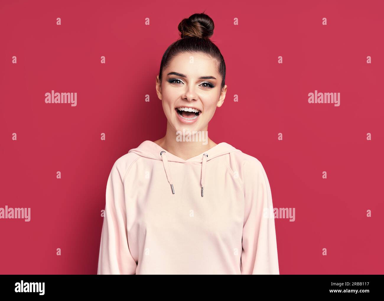 Portrait en tête de jeune femme heureuse souriant et regarde caméra sur fond rose Banque D'Images