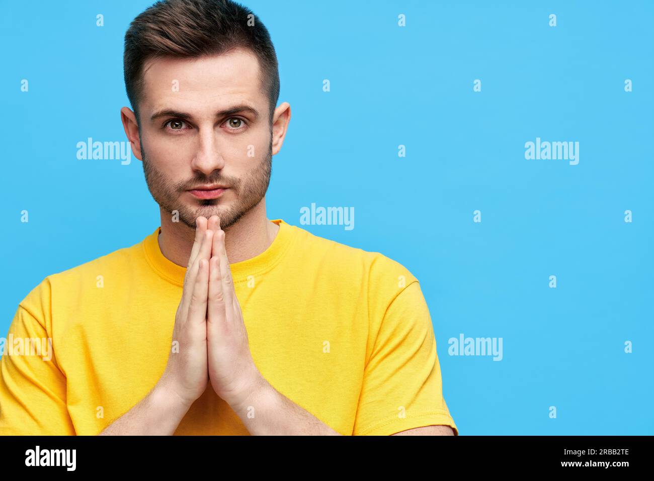 Portrait de l'homme beau avec les mains de prière regardant l'appareil photo avec l'espace de copie sur fond bleu Banque D'Images