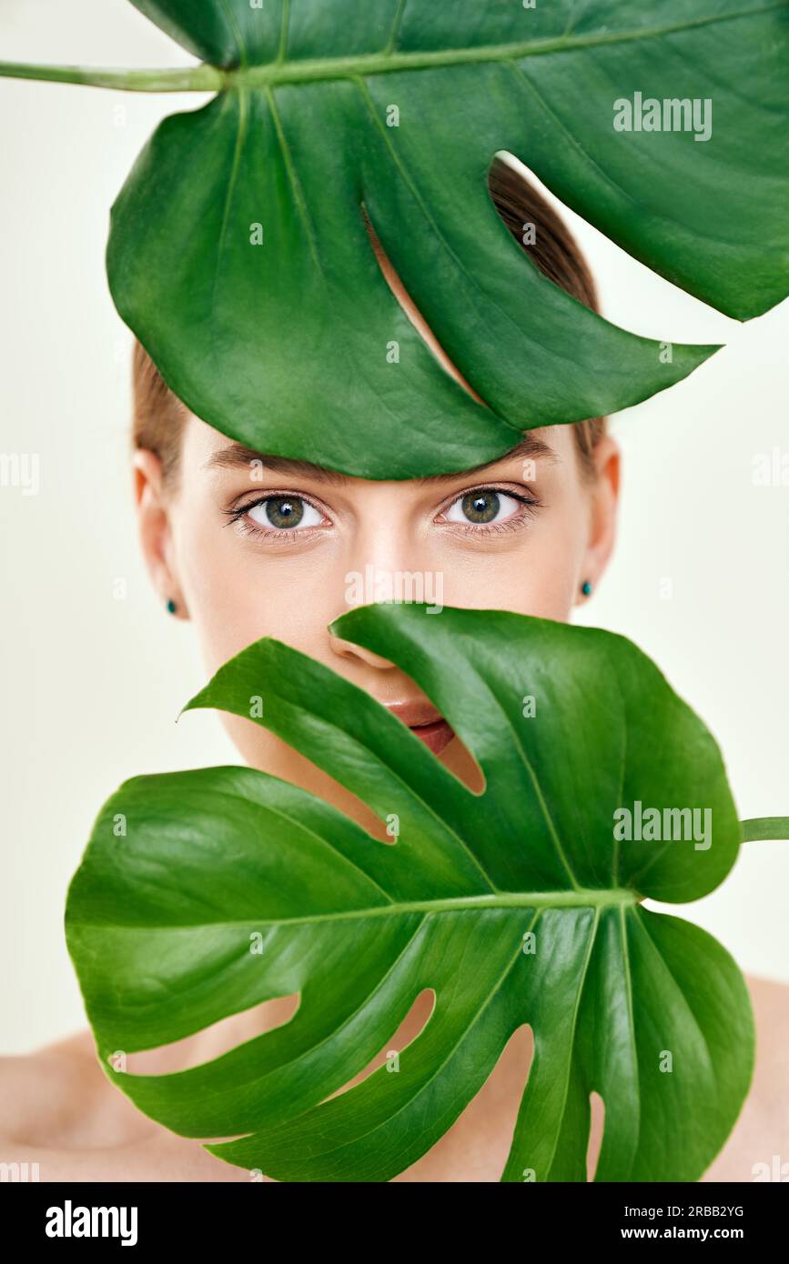 Gros plan de jeune belle femme avec une peau parfaitement lisse se cachant dans les feuilles tropicales. Cosmétiques naturels, soins de la peau, concept spa Banque D'Images