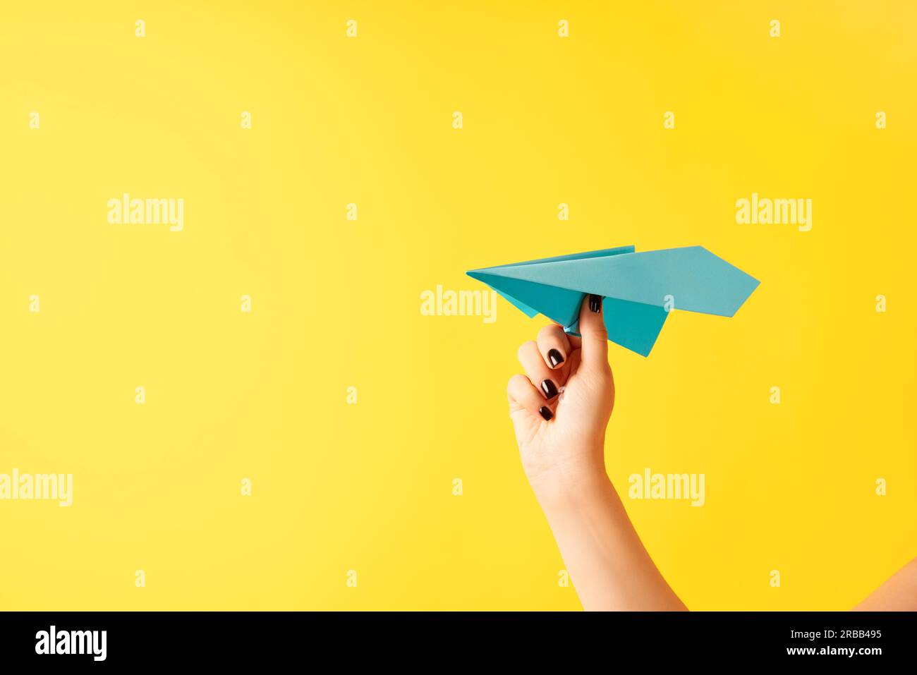 La main d'une femme tient un avion en papier bleu sur fond jaune avec un espace de copie Banque D'Images