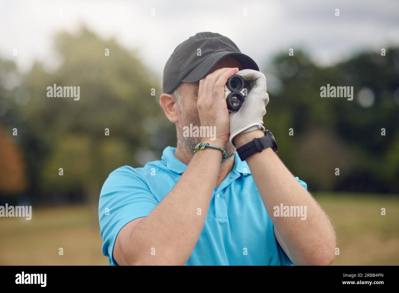 Golfeur utilisant un télémètre pour mesurer la distance jusqu'au trou en le tenant à son œil pendant qu'il regarde le long du fairway dans une tête et des épaules rapprochées Banque D'Images