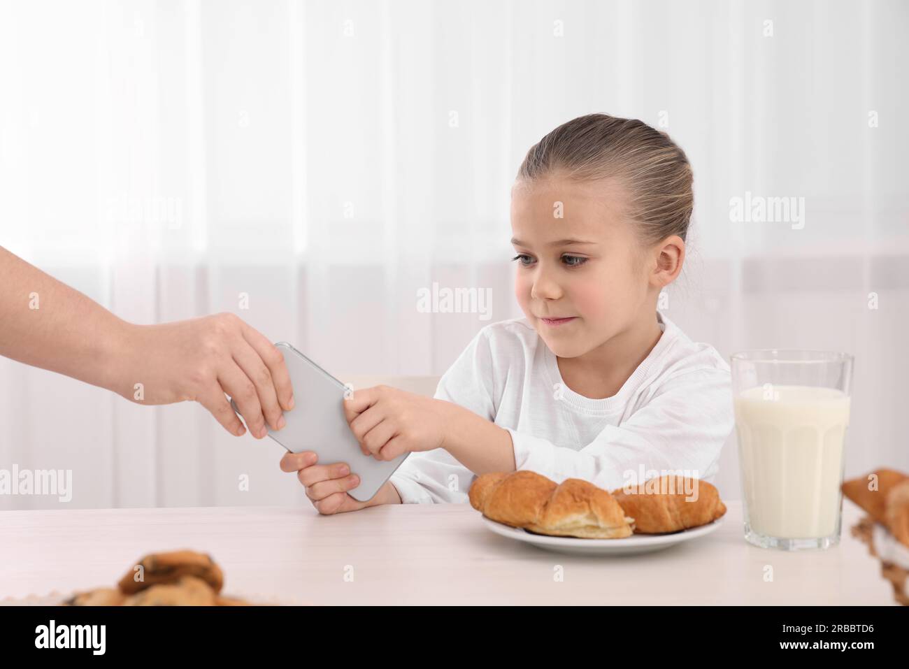 Femme emportant smartphone de sa fille à la table à l'intérieur, gros plan. Addiction à Internet Banque D'Images