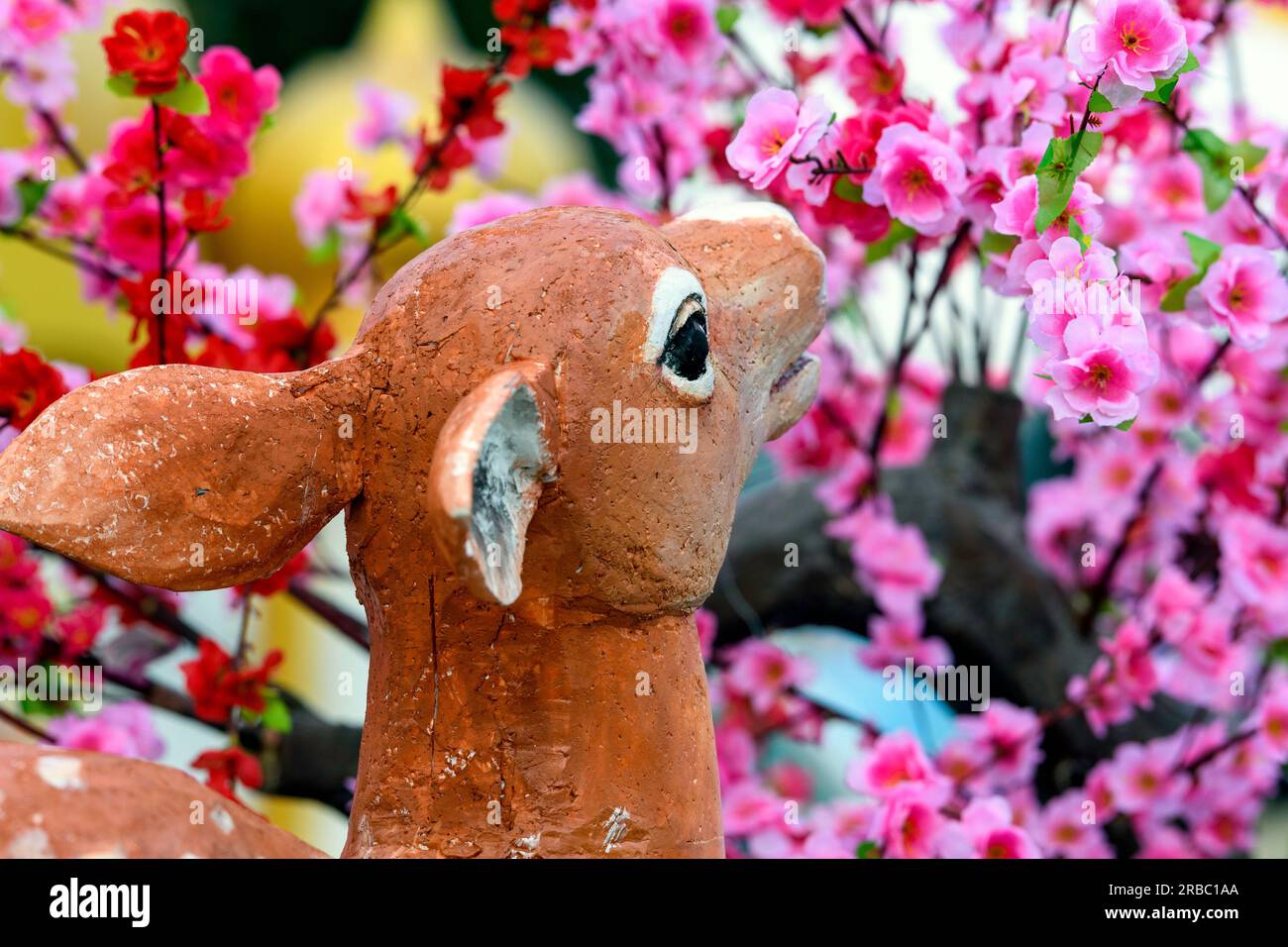 Fauve ou biche pelouse ou ornement de jardin mangeant des fleurs roses Banque D'Images