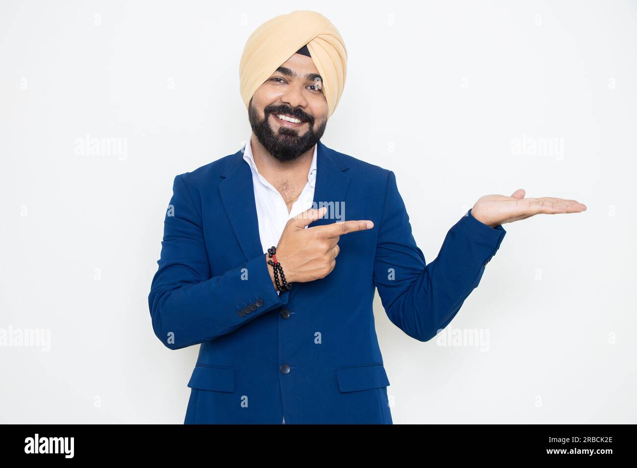 Heureux homme d'affaires sikh indien portant un costume pointant vers les mains vides isolé sur fond blanc. Regardez ici, Publicité et promotion. Banque D'Images