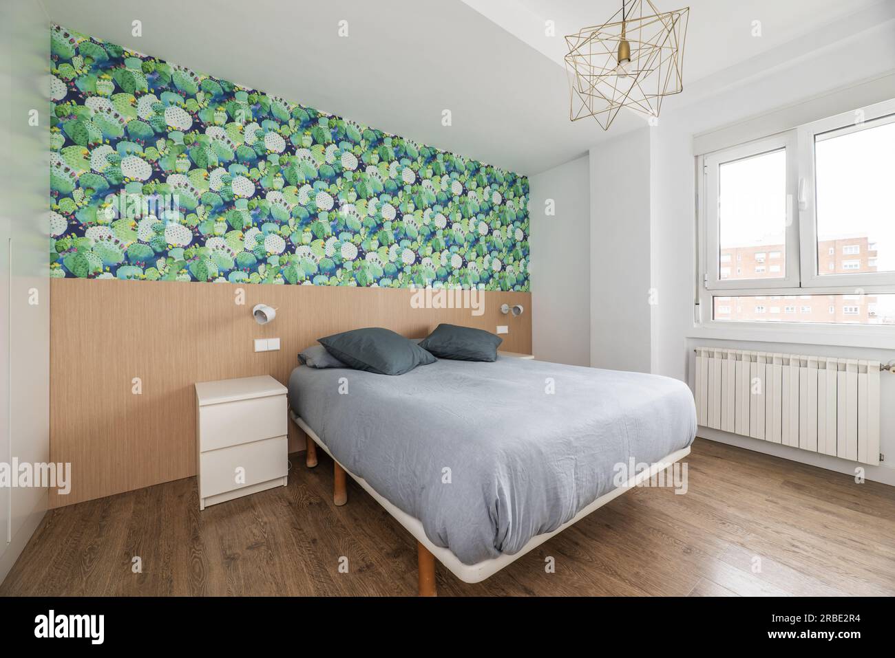 Chambre double avec un lit avec une couette grise, un grand radiateur en aluminium et un mur avec du bois et du papier décoratif Banque D'Images