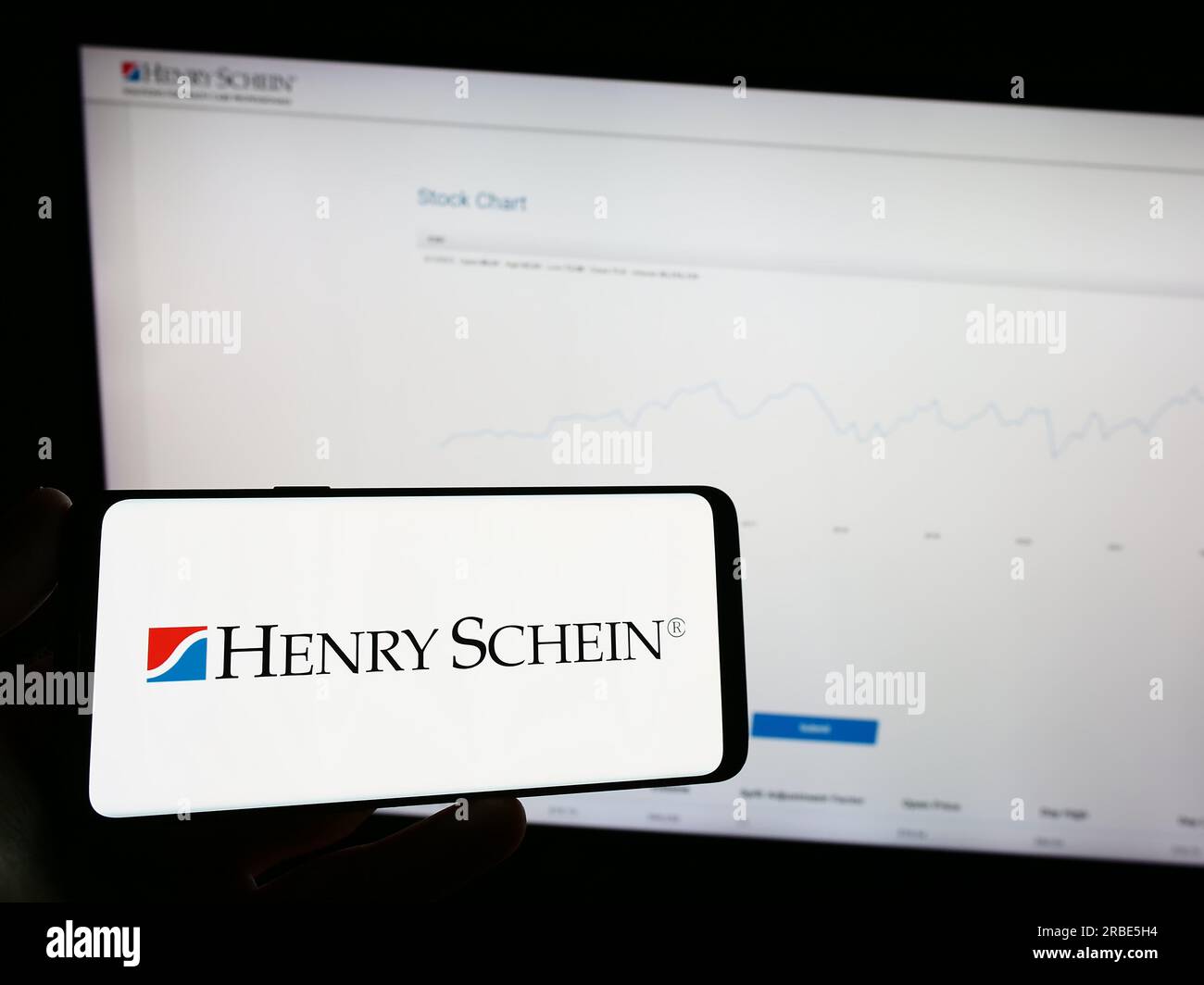 Personne tenant un téléphone portable avec le logo de la société américaine de produits de santé Henry Schein Inc. Sur l'écran devant la page Web. Concentrez-vous sur l'affichage du téléphone. Banque D'Images