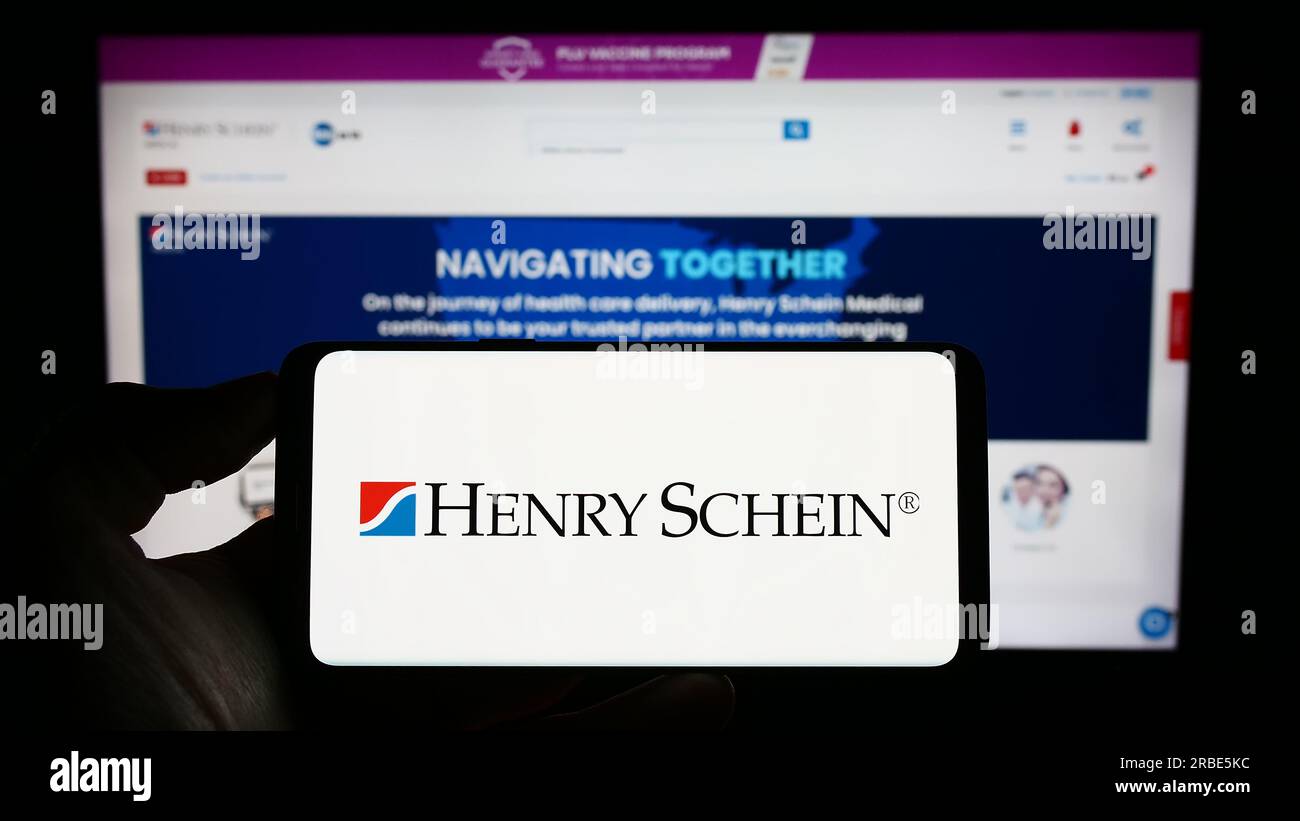 Personne tenant le téléphone portable avec le logo de la société américaine de produits de santé Henry Schein Inc. Sur l'écran devant la page Web. Concentrez-vous sur l'affichage du téléphone. Banque D'Images