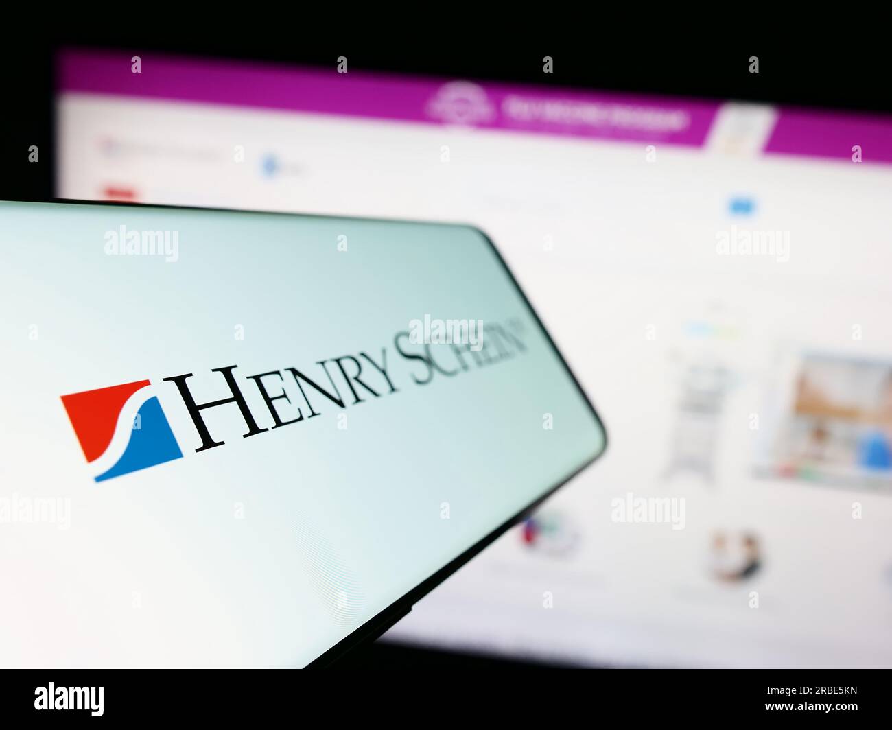 Téléphone portable avec logo de la société américaine de produits de santé Henry Schein Inc. Sur l'écran en face du site Web. Effectuez le focus sur la gauche de l'écran du téléphone. Banque D'Images