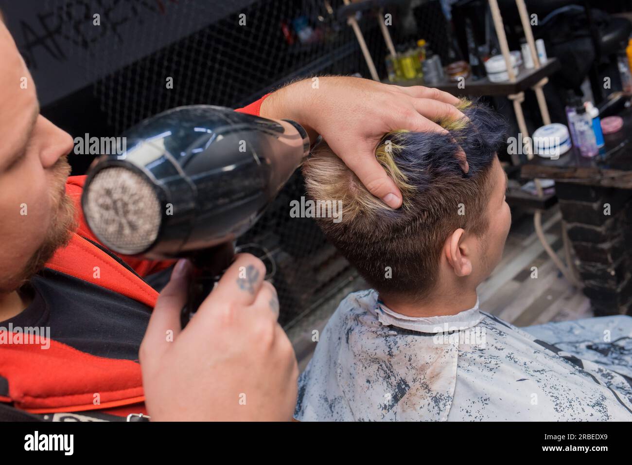 Barber man adulte gros plan soufflage cheveux de jeune client dans le processus de salon de coiffure. Banque D'Images