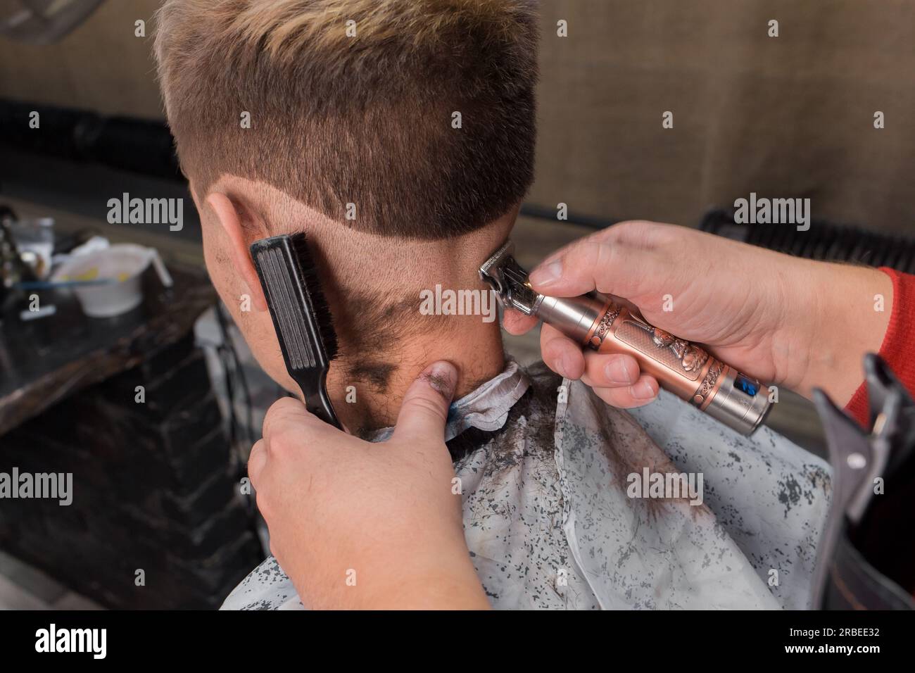 Les mains d'un travailleur de salon professionnel hommes coupent le dos de la tête d'un jeune client des services de coiffure. Banque D'Images