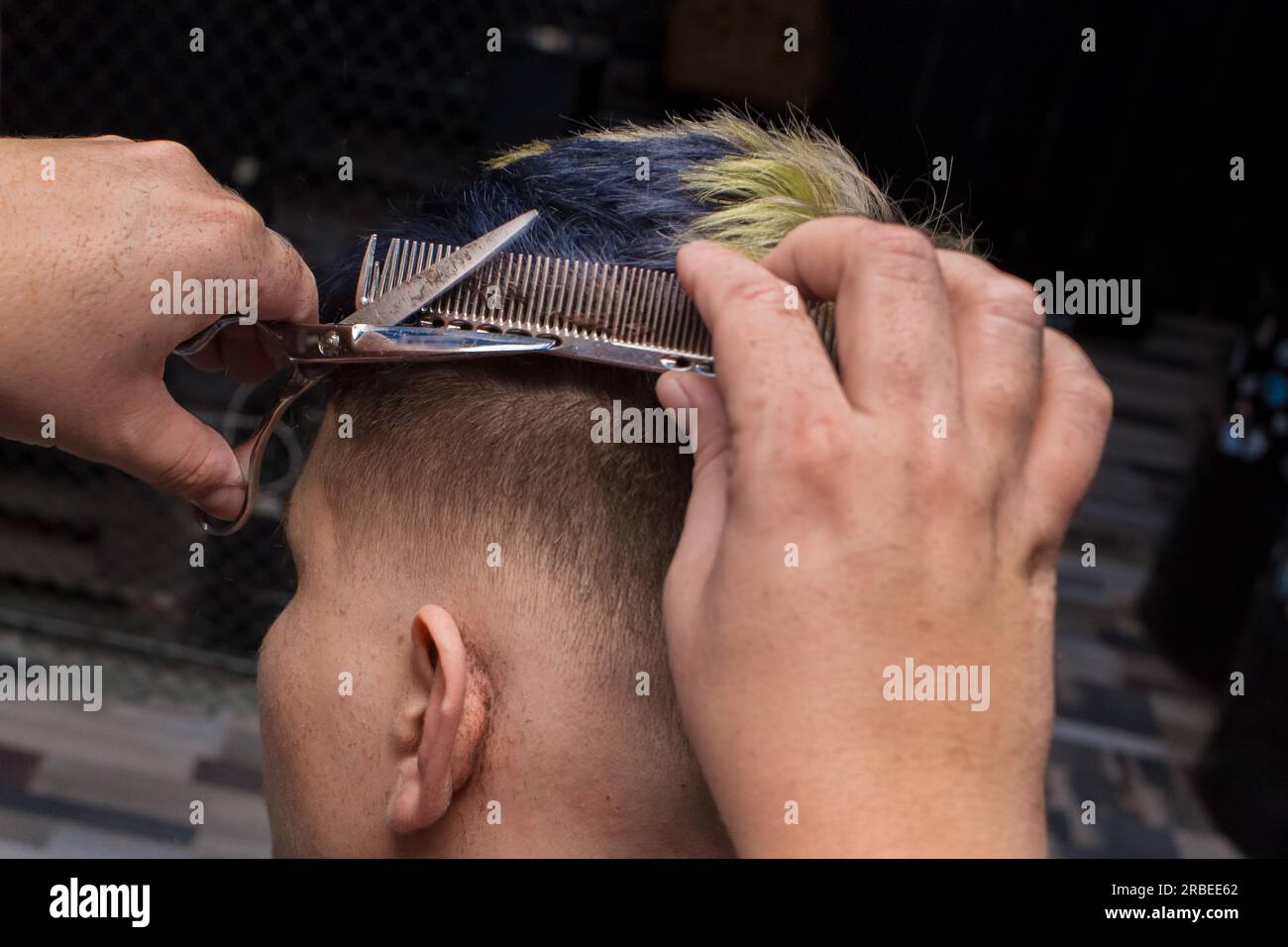 Gros plan les mains d'un maître de salon expérimenté, les hommes font une coupe de cheveux à la mode pour un client, un gars avec des ciseaux et un peigne. Banque D'Images