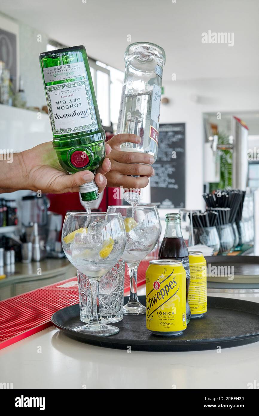 Barman préparant plusieurs cocktails dans un bar, en versant des boissons alcoolisées, du gin et de la vodka, dans de grands verres prêts à mélanger avec des sodas Banque D'Images