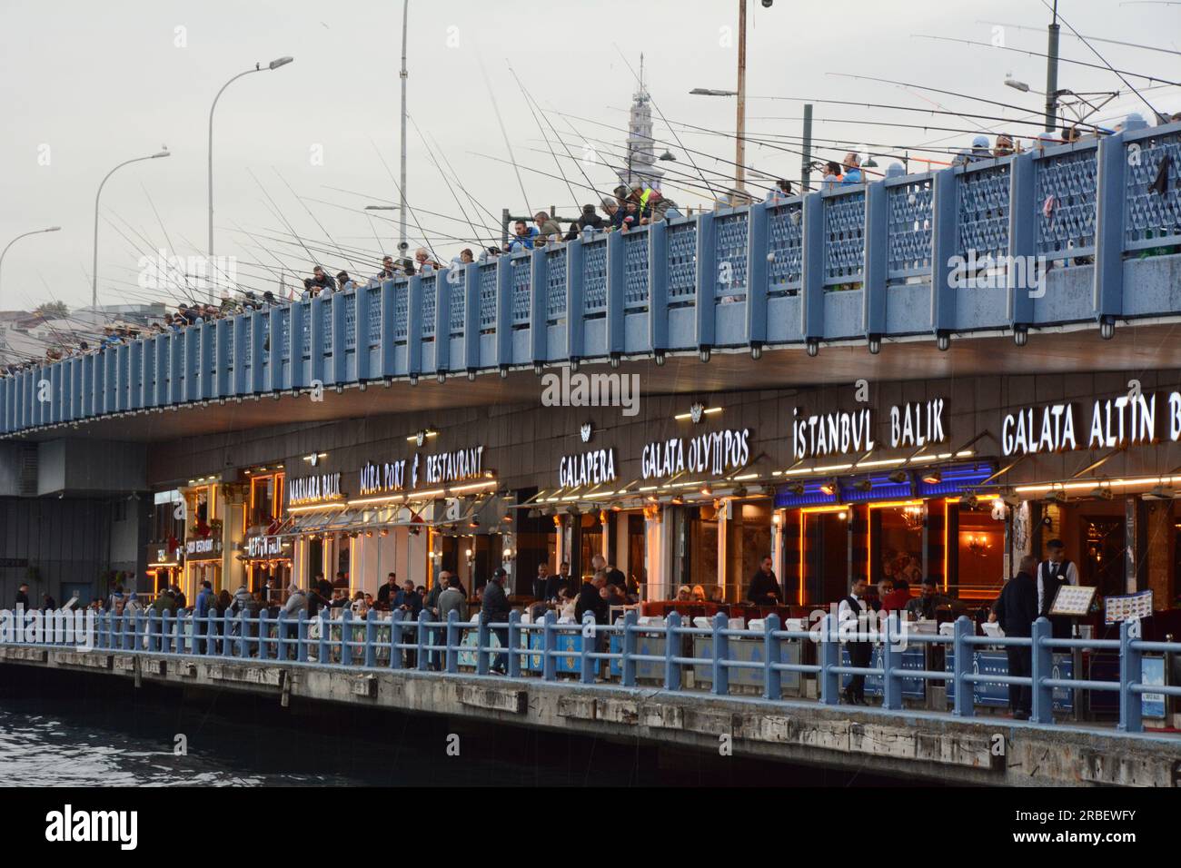 Une ligne de restaurants turcs et de pêcheurs pêchant le long du pont de Galata sur la Corne d'Or et le détroit du Bosphore, Istanbul, Turquie / Turkiye. Banque D'Images