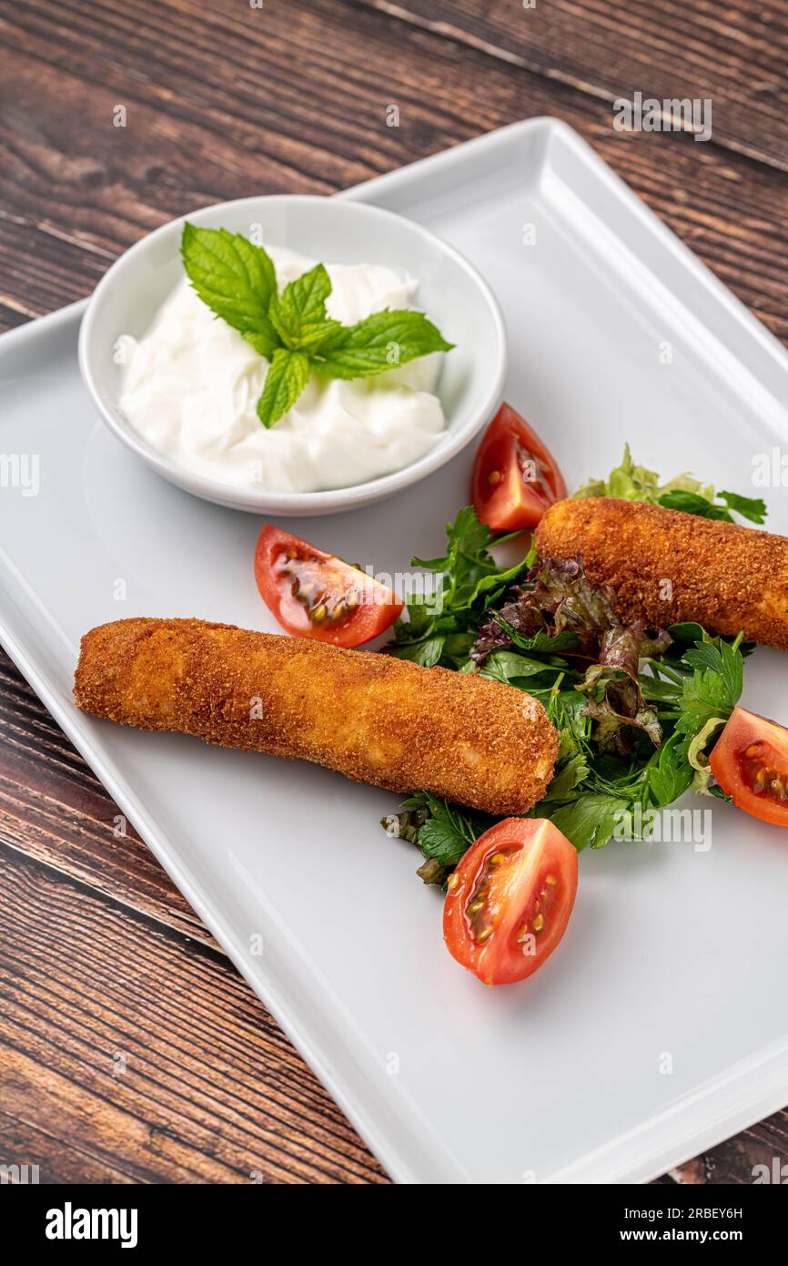 Bâtonnets de mozzarella avec des légumes verts et de la sauce sur une assiette en porcelaine blanche Banque D'Images