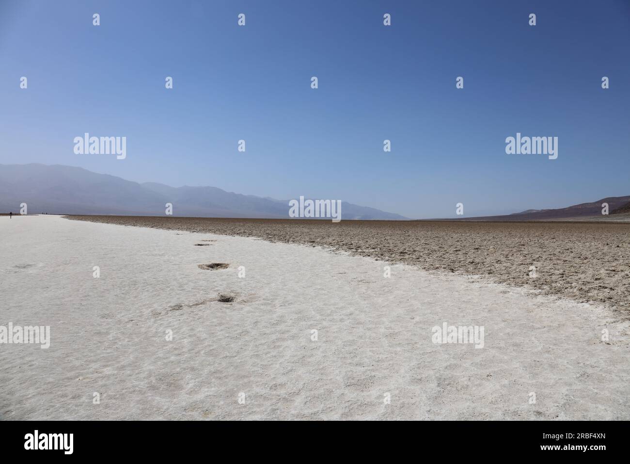 Les marais salants du bassin Badwater s'étendent à l'horizon avec des montagnes au loin, couvertes de brume, dans le parc national de la Vallée de la mort, Calif Banque D'Images