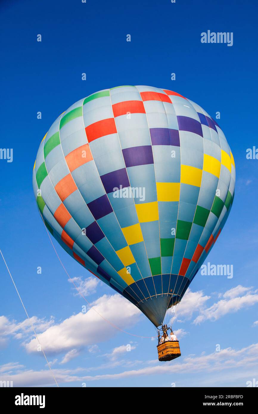 Belle montgolfière colorée contre un ciel bleu profond et des nuages blancs volant dans la lumière du matin. Banque D'Images