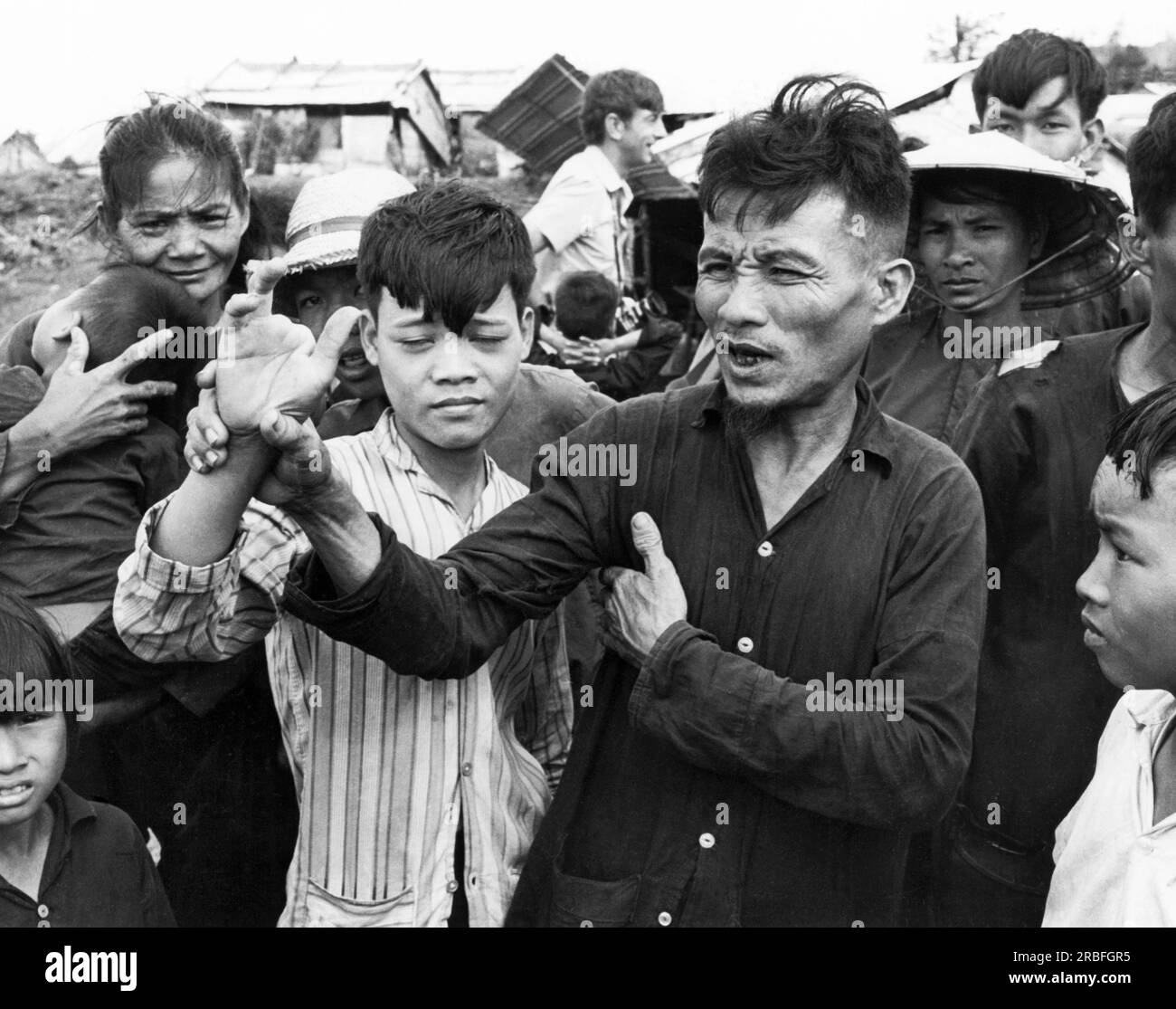 Song My, Vietnam: 19 novembre 1969 le paysan sud-vietnamien Do CHUC tient la main mutilée de son fils Do Ba, alors qu'il raconte aux journalistes du centre de réinstallation Song My Settlement le meurtre de 370 civils dans le hameau de Tu Cung, connu sous le nom de massacre de My Lai. Le garçon de quatorze ans a reçu une balle dans le cou et a perdu deux doigts tandis que son père a reçu une balle dans le cou. Banque D'Images