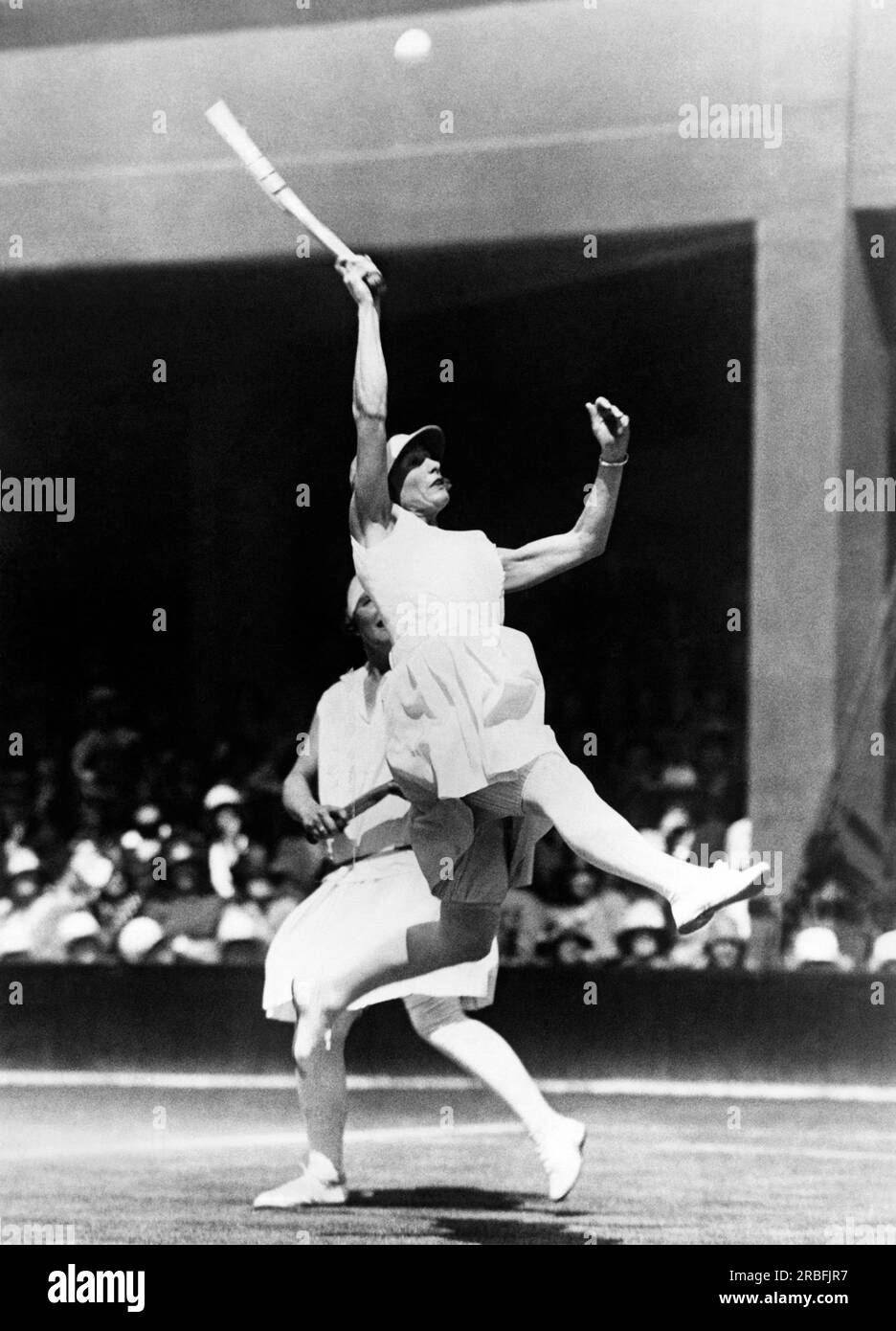 Londres, Angleterre : 1928 Kea Bouman des pays-Bas saute haut pour essayer de retourner un ballon haut en quarts de finale de double à Wimbledon. Son partenaire est la joueuse britannique Evelyn Colyer. Banque D'Images
