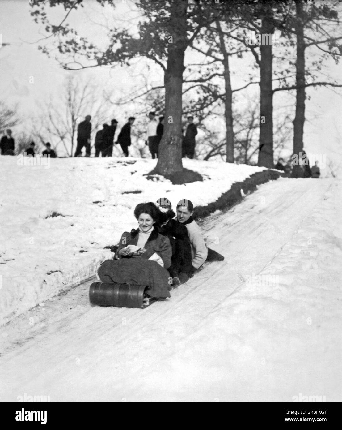 États-Unis : c. 1900 Une femme en robe de style victorien avec deux amis masculins descendant une colline sur un toboggan. Banque D'Images