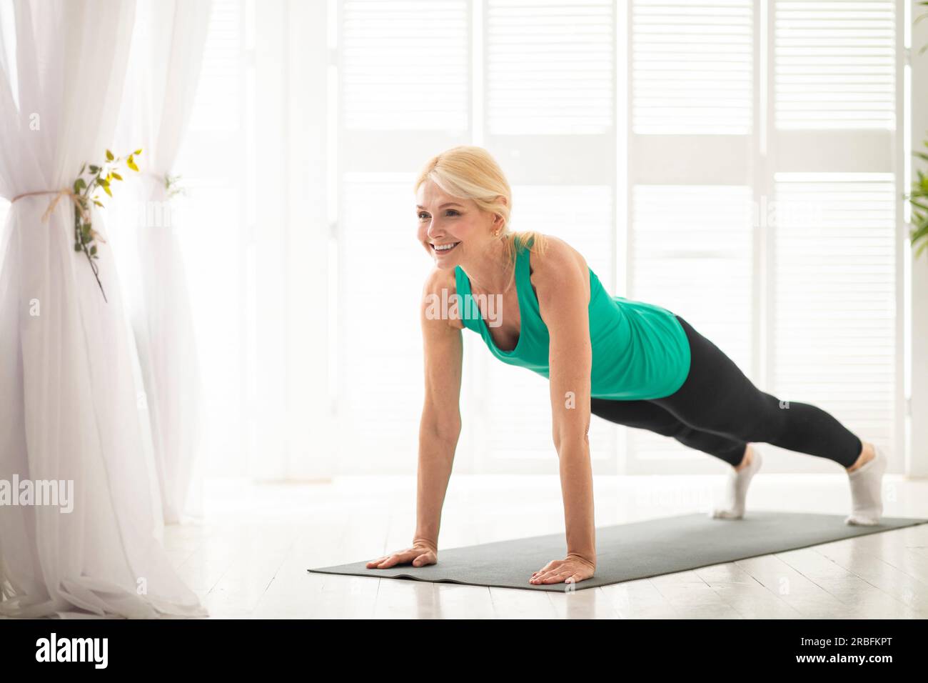 Entraînement domestique. Sportive femme d'âge moyen faisant l'exercice de planche à la maison Banque D'Images