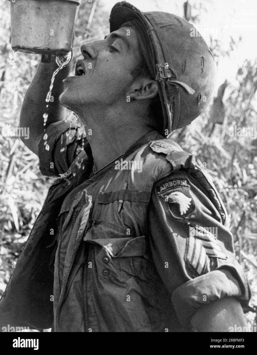 Vietnam : avril 1968 Un 101st Airborne sargeant a du mal à boire de l’eau dans une tasse de cantine qui avait été perforée par un fragment de coquille. Banque D'Images