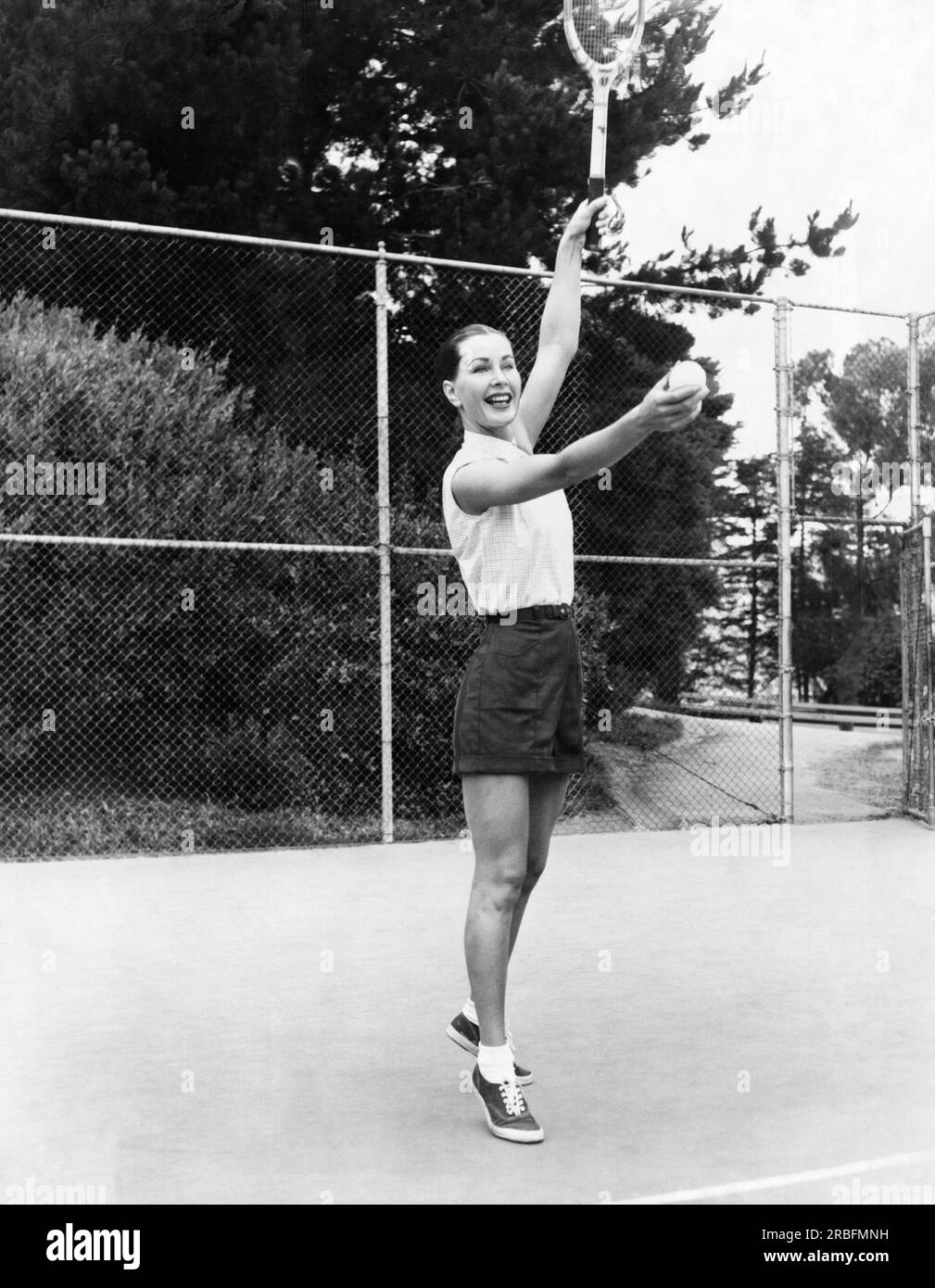 San Francisco, Californie : juin, 1953 le mannequin Evelyn Frey se prépare à servir avec le sourire dans une publicité de jeu de tennis pour Joseph Magnin. Elle porte une chemise en coton à carreaux, 4,95 $ et un short en gabardine, 3,95 $. Banque D'Images