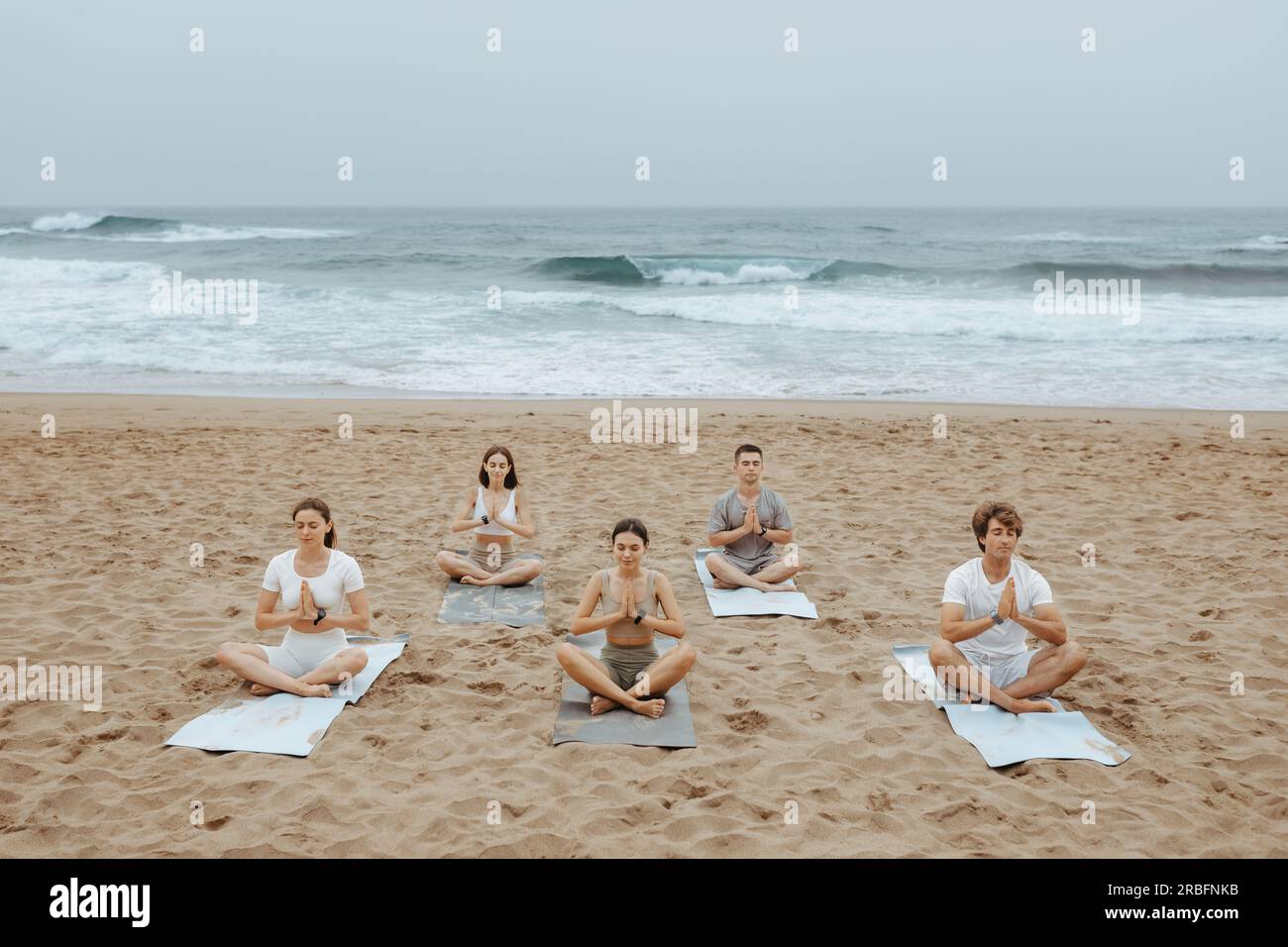 Vue ci-dessus d'un groupe de femmes et d'hommes pratiquant le yoga à la plage sur la rive de l'océan, assis sur des nattes et méditant Banque D'Images