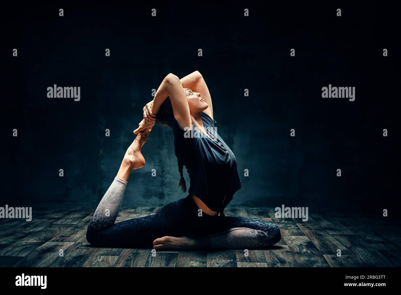 Young woman practicing yoga procédant d'une pattes pigeon king poser dans une pièce sombre. Eka Pada Rajakapotasana asana. Le bien-être et mode de vie sain Banque D'Images