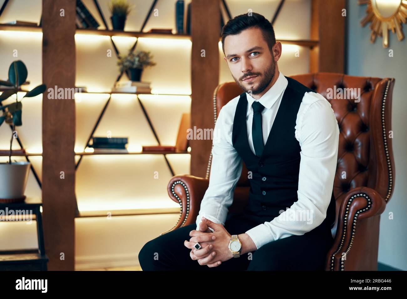 Beau jeune homme assis et posant dans un fauteuil à l'intérieur de luxe moderne. Fashion portrait Banque D'Images