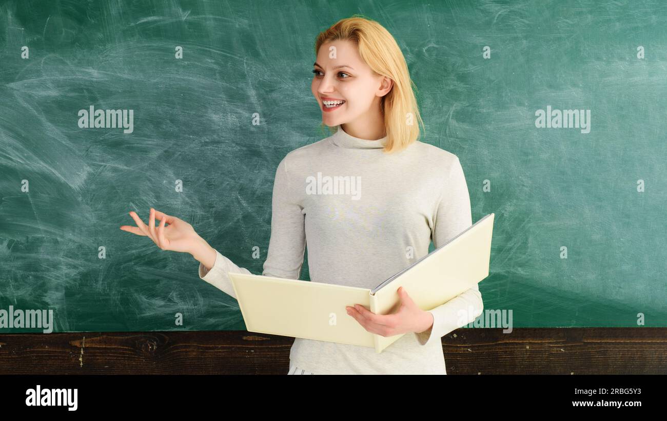 L'éducation au lycée universitaire. Retour à l'école. Journée mondiale des enseignants. Enseignante souriante avec cahier debout près du tableau noir donnant Banque D'Images