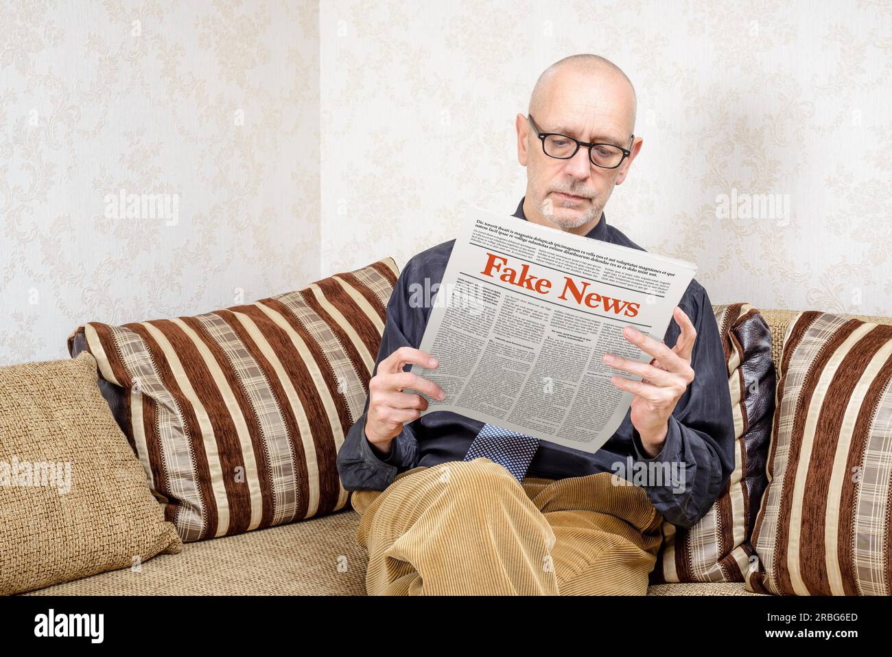 Un homme portant des lunettes est assis sur un canapé à la maison, la lecture du journal de faux rapports news Banque D'Images