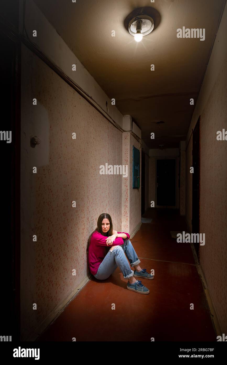 Une femme triste et désespérée est assise dans un couloir sombre éclairé par une lumière sombre. Sa douleur et ses nombreux problèmes l'ont poussée dans un isolement complet. Banque D'Images