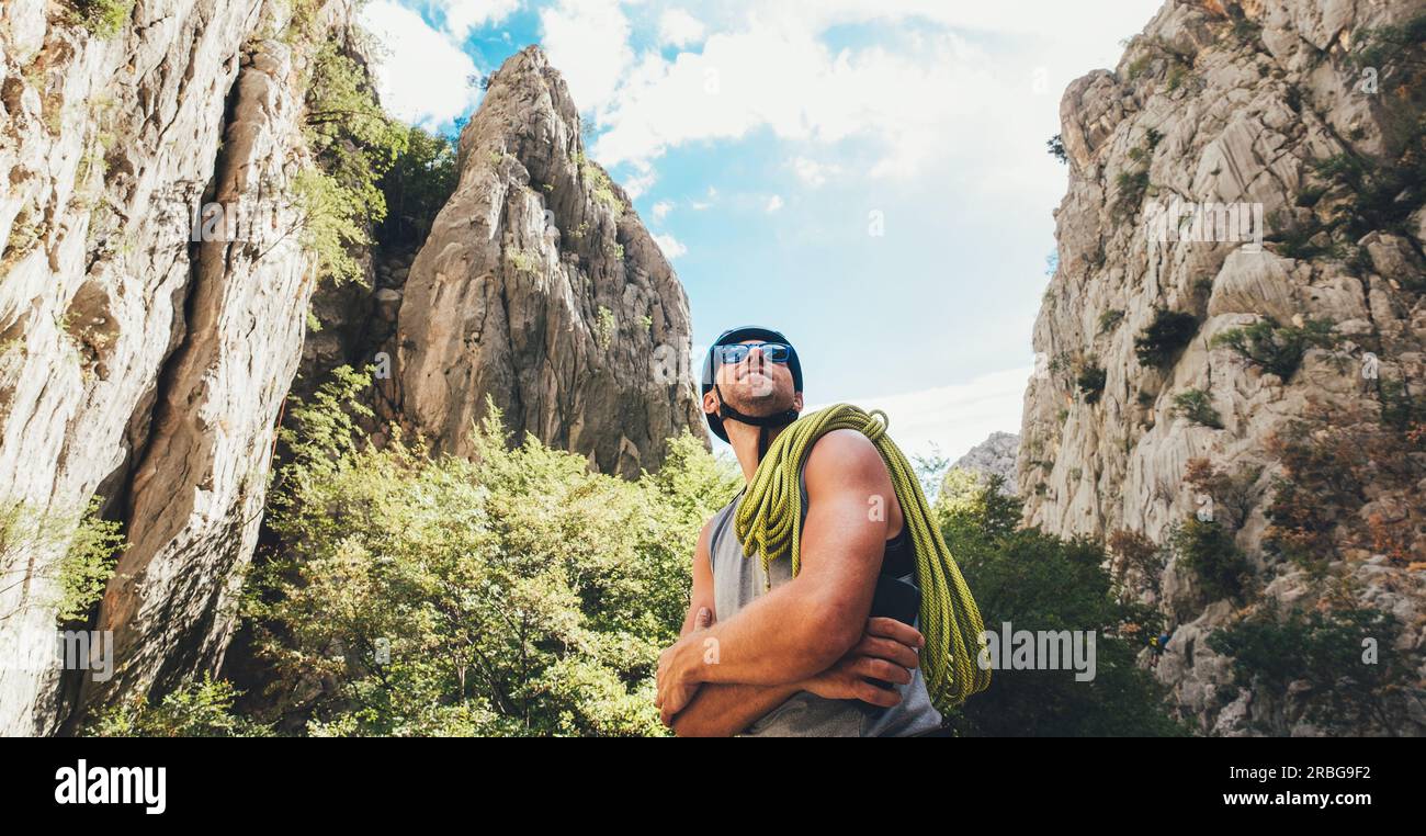 Portrait d'un grimpeur souriant dans un casque de protection et des lunettes de soleil avec corde d'escalade sur l'épaule debout dans le parc Paklenica entre la falaise de roche W Banque D'Images