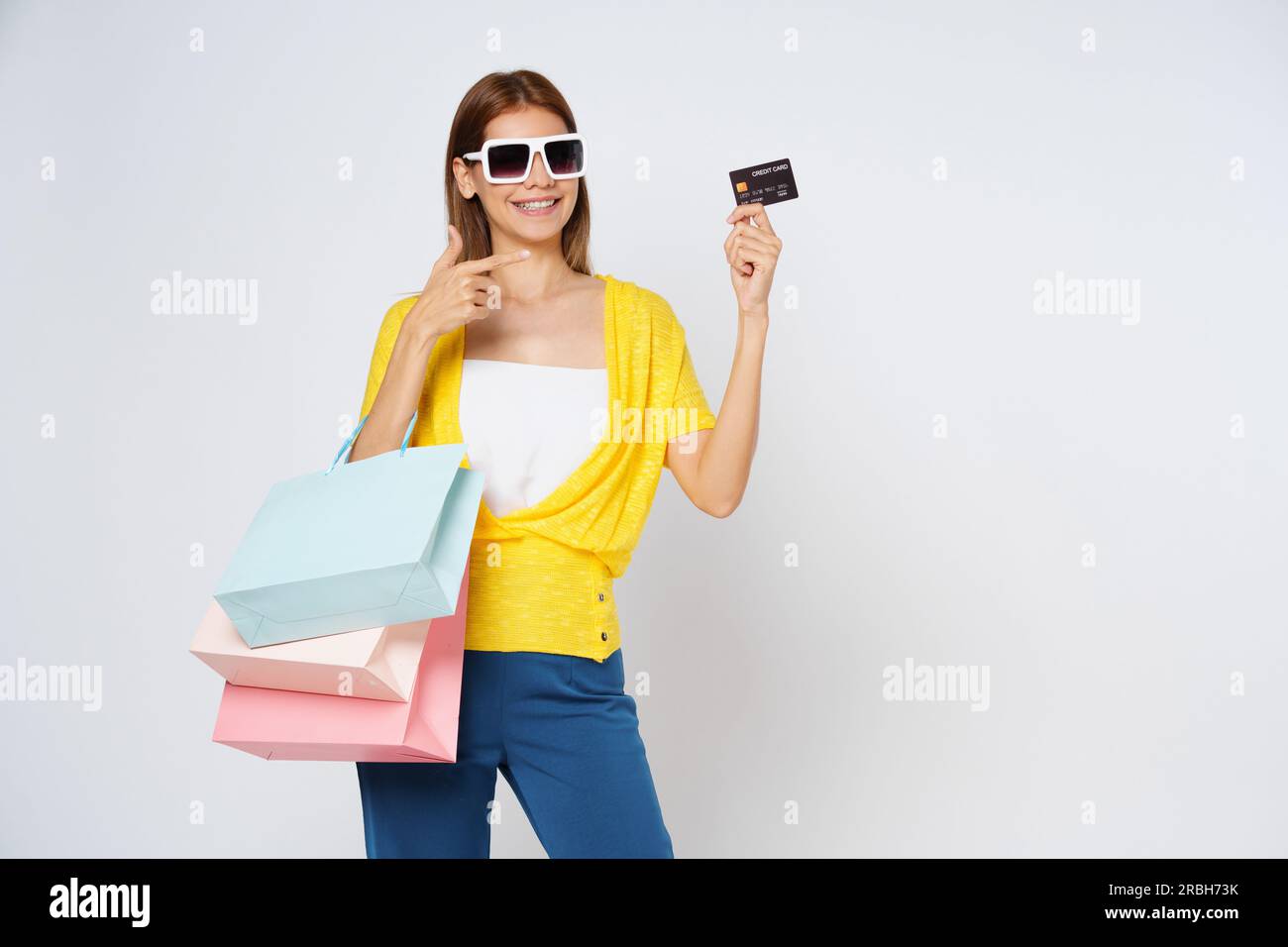 Bonne jeune femme tenant des sacs de shopping et montrant carte de crédit isolée sur fond blanc. Banque D'Images
