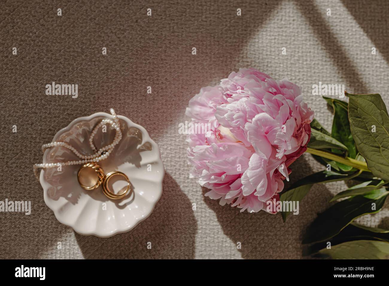 Composition nature morte avec pivoine rose et bijoux dans une petite assiette à la lumière naturelle Banque D'Images