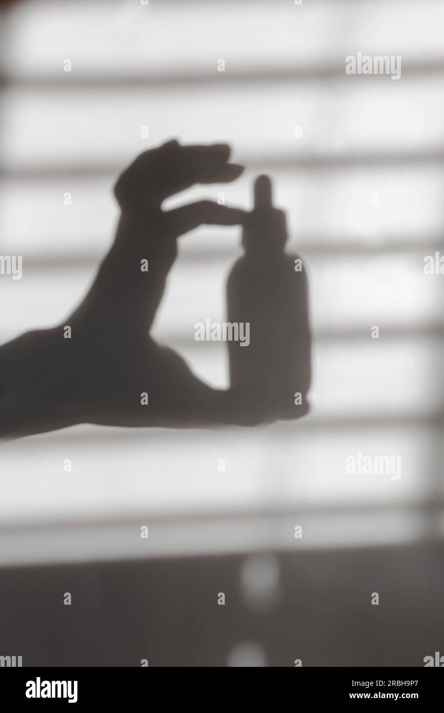 Silhouette d'ombre de la main féminine tenant bouteille de sérum, concept de beauté Banque D'Images