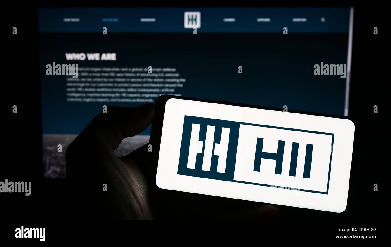 Personne tenant le smartphone avec le logo de la société de construction navale américaine HII Corporate sur l'écran en face du site Web. Concentrez-vous sur l'affichage du téléphone. Banque D'Images