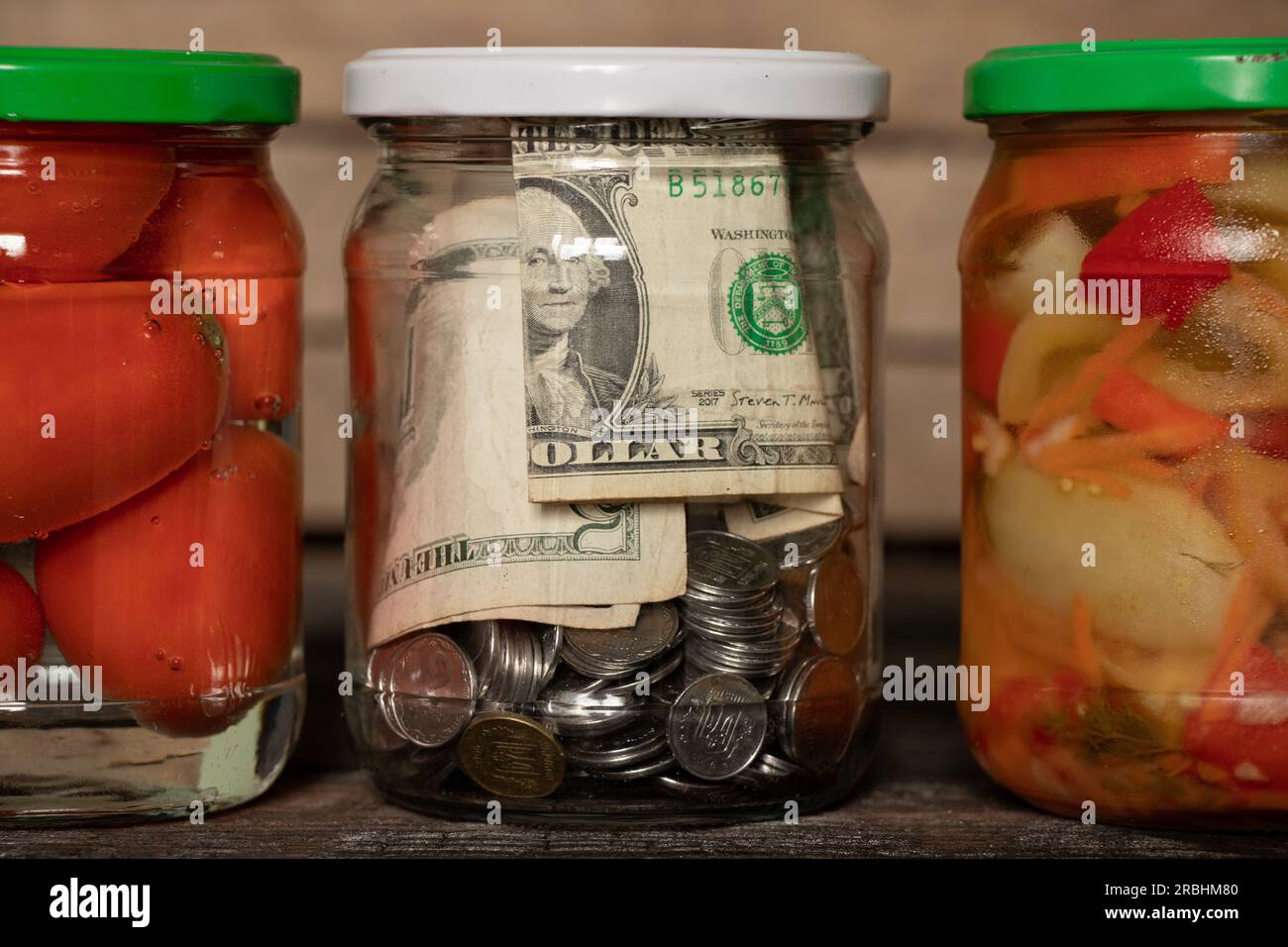 les dollars et les pennies fermés dans un pot en verre se tiennent à côté des légumes en conserve à la maison sur une étagère, économiser des finances, de l'argent dans une boîte, le thème financier, faire Banque D'Images