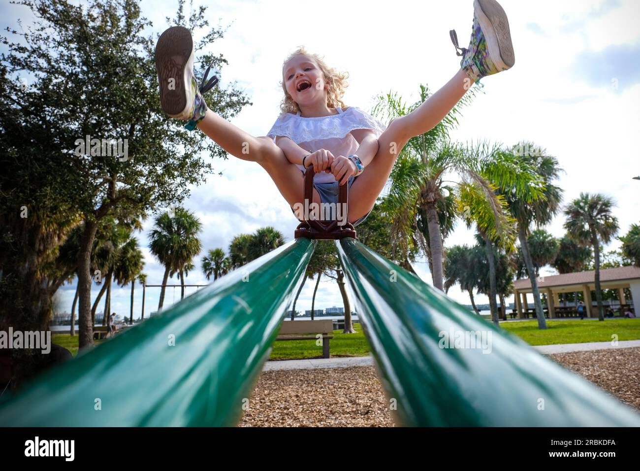 fille jouant sur la balançoire avec les jambes en l'air dans un parc sur la journée ensoleillée Banque D'Images