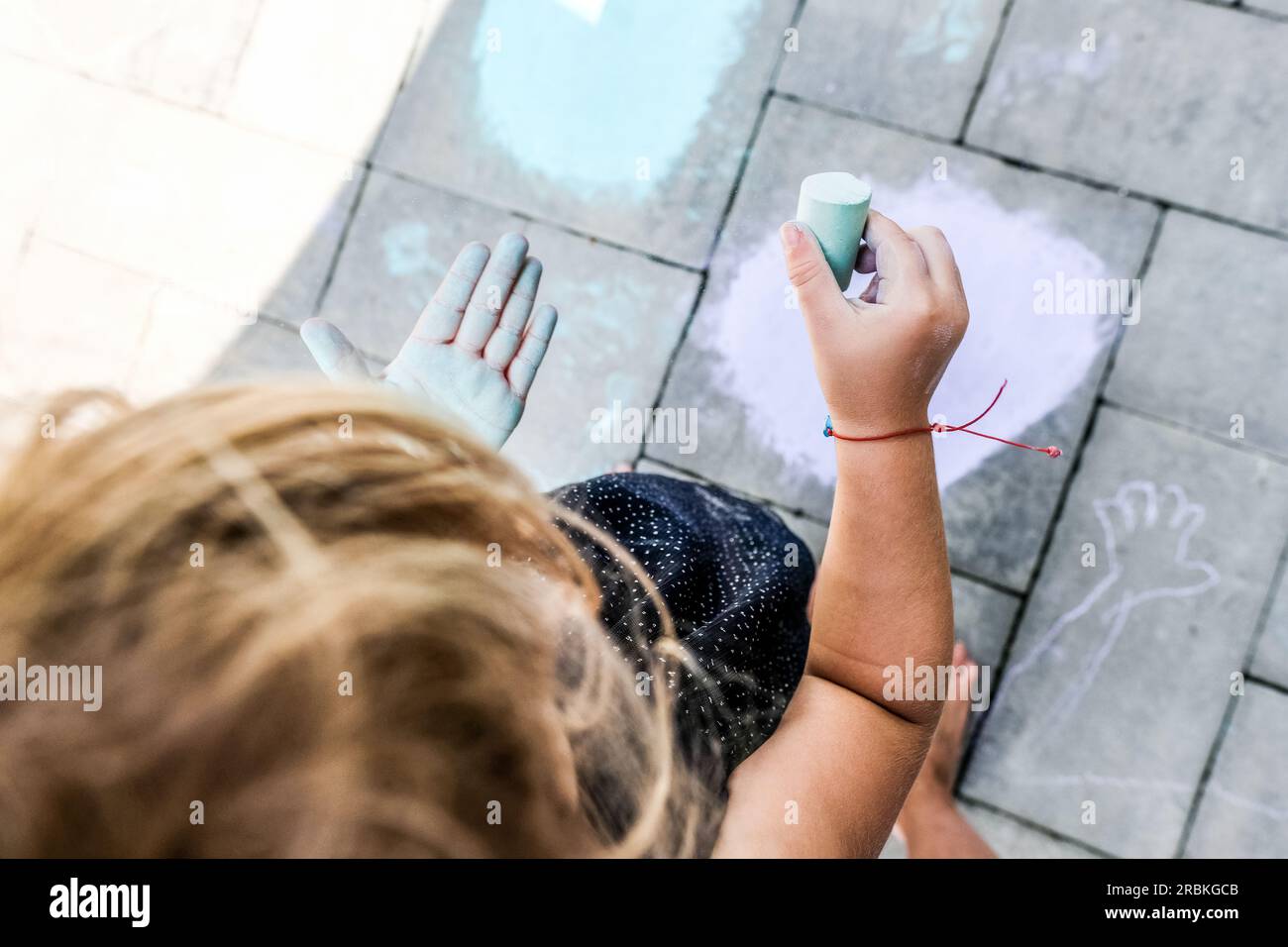 petite fille jouant avec de la craie à l'extérieur sur la main de couleur de patio au soleil Banque D'Images