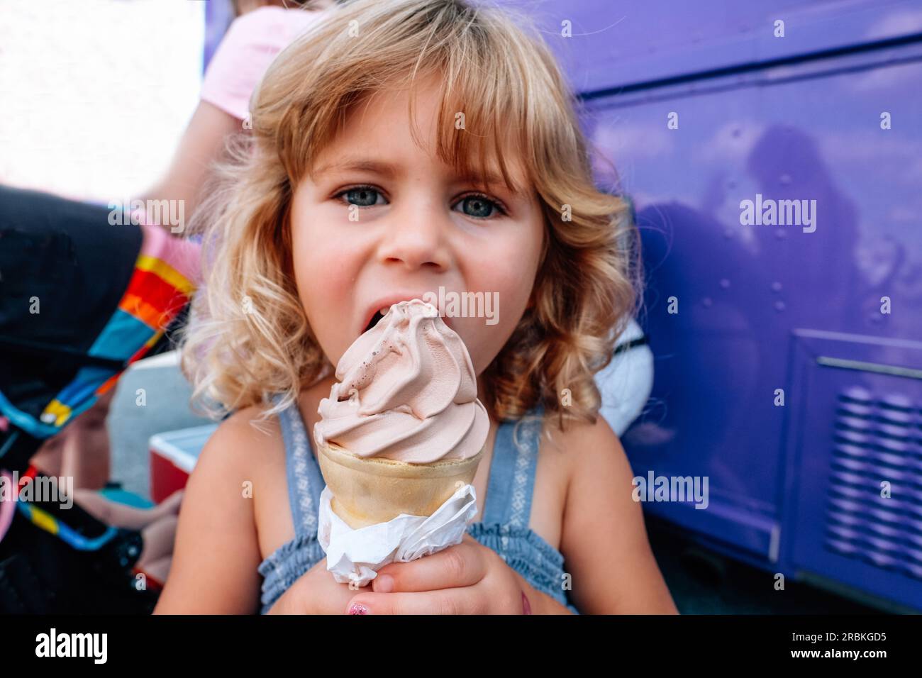 portrait environnemental de petite fille mangeant le cône de crème glacée à l'extérieur Banque D'Images